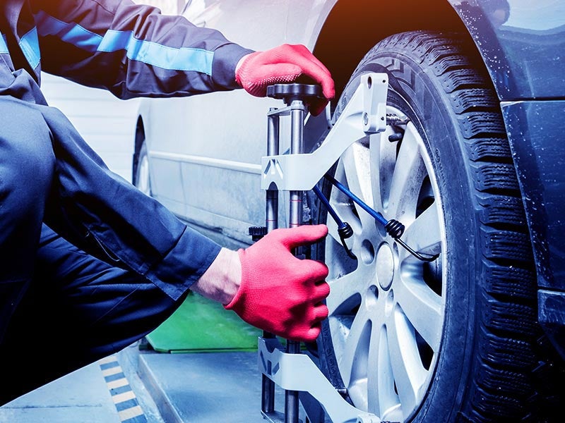 A mechanic in red gloves attaches a wheel alignment tool to a car's tire.